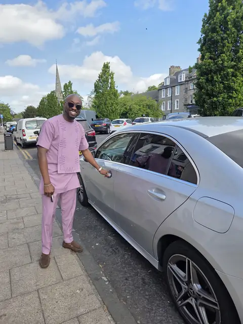 Oluseyi in a pink two-piece beside a silver car