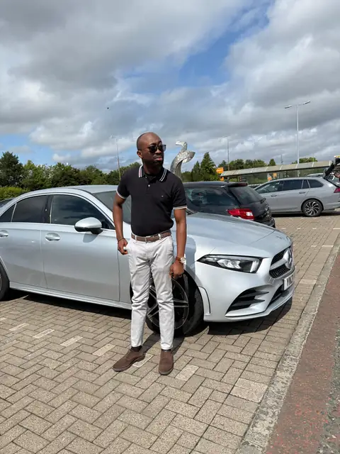 Oluseyi in a black polo beside a white car