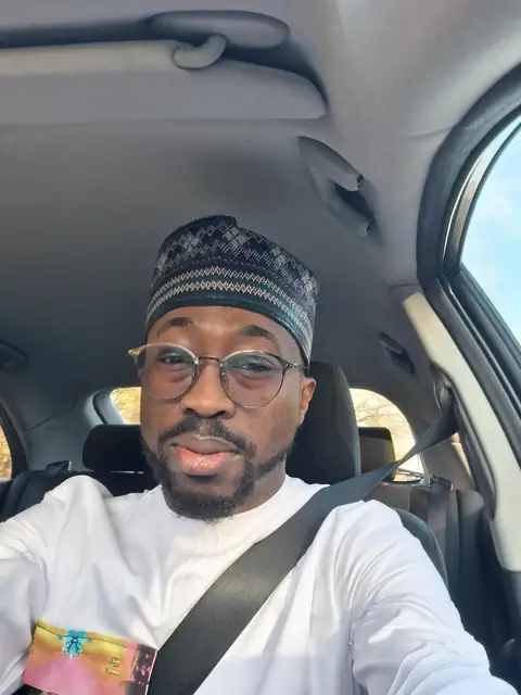 Oluseyi in a patterned cap, smiling in the car